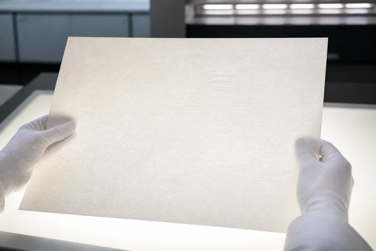 Mains gantées de blanc examinant une feuille imprimée vierge en lumière rasante au-dessus d&rsquo;une table de contrôle d&rsquo;atelier
